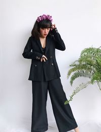 Portrait of smiling young woman wearing black suits standing against plants over white background 
