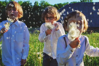 Friends blowing dandelions while standing on grassy field