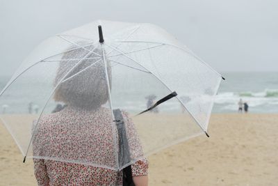 Rear view of woman with umbrella standing on beach