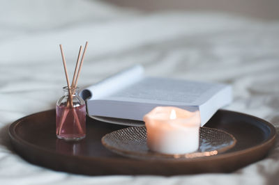 Home liquid fragrance in glass bottle with wooden sticks and scent candle with open paper book