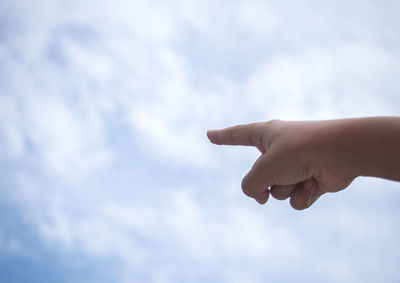 Cropped hand of person pointing against cloudy sky