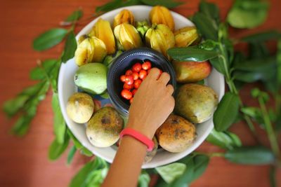 Close-up of hand holding fruits in plate on table