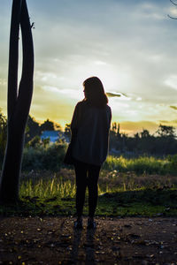 Rear view of silhouette woman standing on field against sky