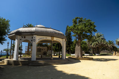 Built structure by trees against blue sky on sunny day