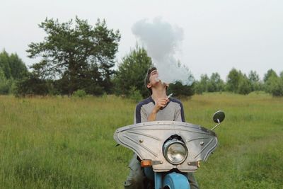 Man smoking hookah while sitting on motorcycle at field