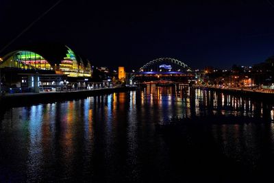 Illuminated bridge over river in city against clear sky at night