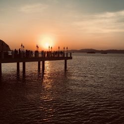 Silhouette wooden posts in sea against sky during sunset