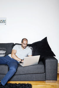 Mid adult man at home using laptop sitting on sofa