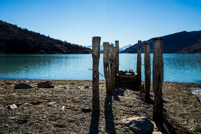 Wooden posts on beach against clear blue sky