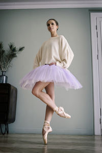 Charming ballerina poses showing her legs in the room in front of the mirror in pointes and tutu