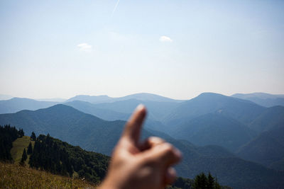 Cropped hand of person pointing at mountain range against sky