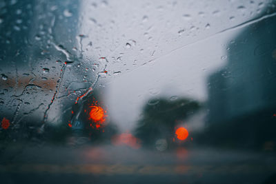 Raindrops on glass window of car with defocused traffic lights in background