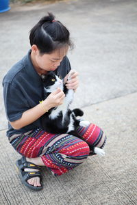 Woman with cat crouching on footpath