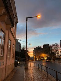 Street amidst illuminated buildings against sky at sunset