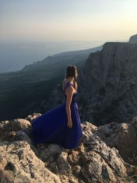 Woman sitting on rock at mountain against sky