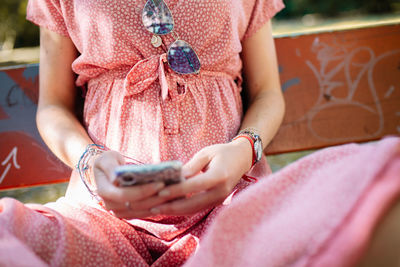 Midsection of young woman using phone while sitting on bench