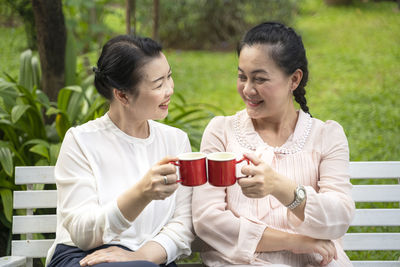 Women toasting coffee cups while sitting on bench