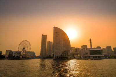 Buildings by river against sky during sunset