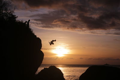 Silhouette man diving in sea by sea against sky during sunset