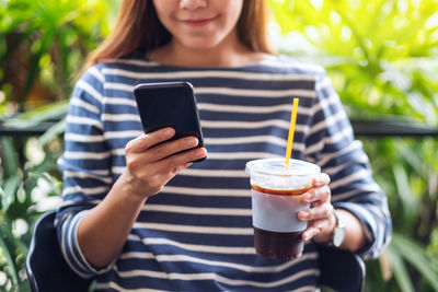 Closeup image of a beautiful young asian woman holding and using smart phone while drinking coffee