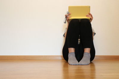 Woman using laptop while sitting on floor against wall