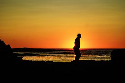 Silhouette man standing on beach against sky during sunset