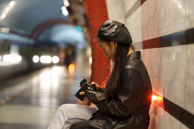 Fashionable asian photographer girl watch picture on camera after walk in city wait for subway train