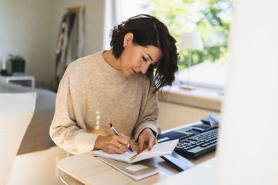 Mature businesswoman writing in note pad on table at home