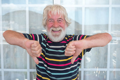 Portrait of senior man showing thumbs down against window