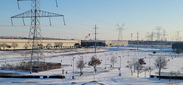 Electricity pylon on snow covered landscape against sky