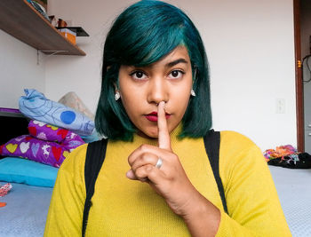 Portrait of young woman with finger on lips sitting on bed