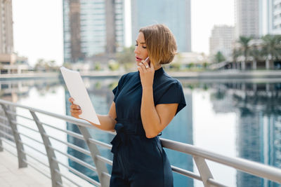 A young female entrepreneur is talking on a smartphone in the city and looking through documents