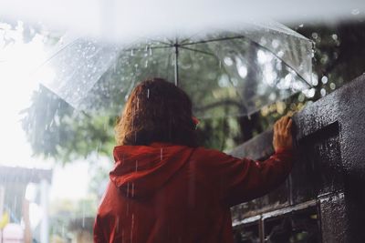 Rear view of woman with umbrella standing by retaining wall during rainfall