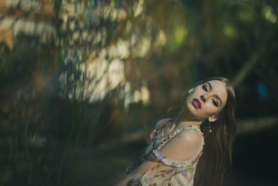 Portrait of beautiful young woman standing against trees in park