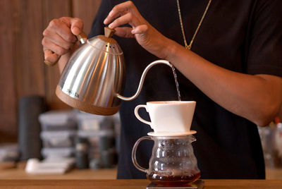 Midsection of woman pouring coffee on table