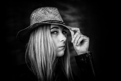 Portrait of young woman wearing hat against black background