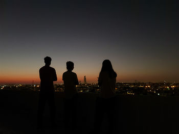 Silhouette people looking at cityscape against sky during sunset