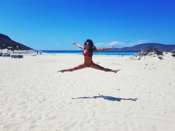 Full length of woman jumping at beach against blue sky