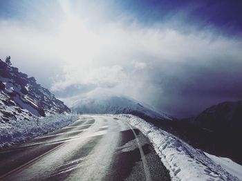 Empty road by mountain against sky during winter