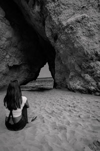 Rear view of woman sitting on sand against rock formation