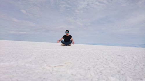 Man wearing sunglasses meditating at salar de uyuni against sky