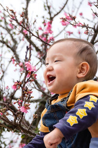 Close-up of baby boy laughing against tree