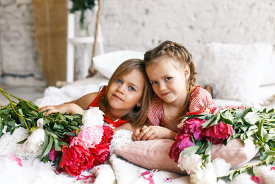 Smiling siblings sitting amidst flowers on bed at home