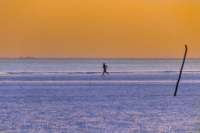 Silhouette person in sea against sky during sunset