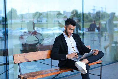 Businessman using digital tablet while sitting on bench outdoors