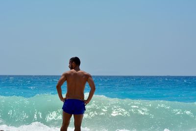 Full length of shirtless man standing on beach against clear sky