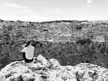 Rear view of woman sitting on rock against cityscape