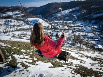 Woman in a rope swing on top of the mountains during winter with a beautiful panoramic view