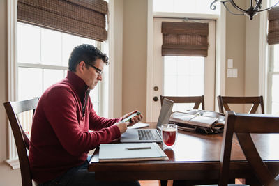 Man in glasses working from home using a computer at a dining table.