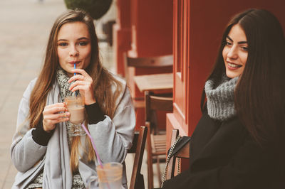 Female friends having drink while sitting at sidewalk cafe